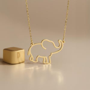 May include: A gold-toned necklace featuring a delicate, open-outline pendant in the shape of an elephant. The pendant is suspended from a thin, matching gold-toned chain. The design consists of a continuous wire-like frame forming the elephant.