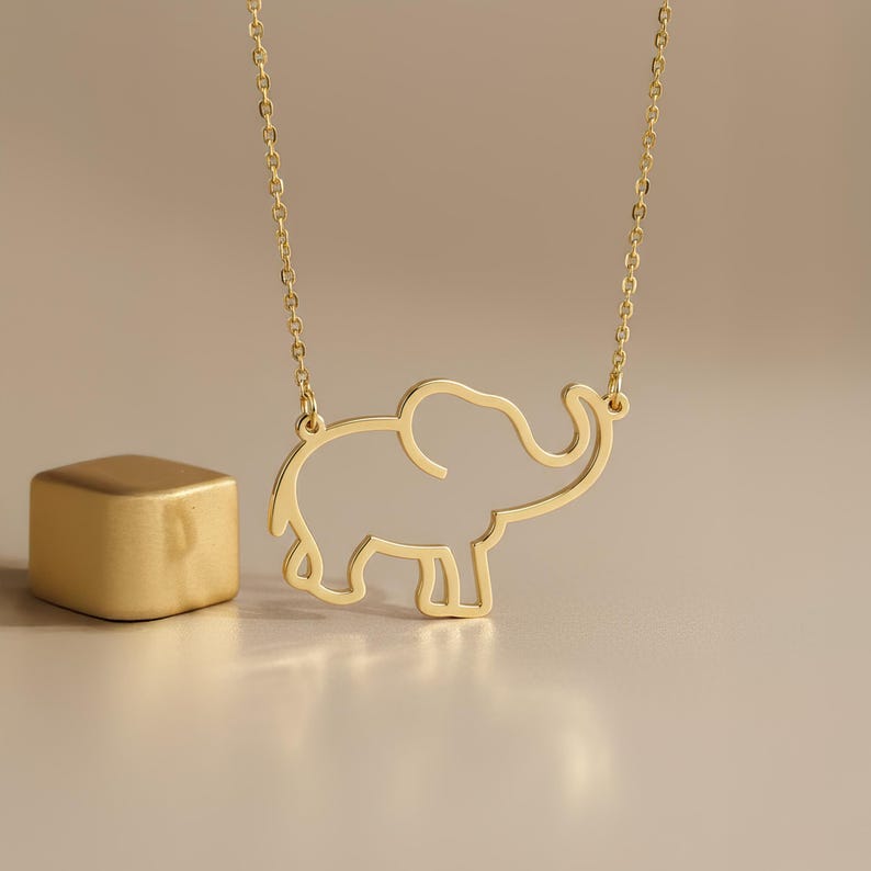 May include: A gold-toned necklace featuring a delicate, open-outline pendant in the shape of an elephant. The pendant is suspended from a thin, matching gold-toned chain. The design consists of a continuous wire-like frame forming the elephant.