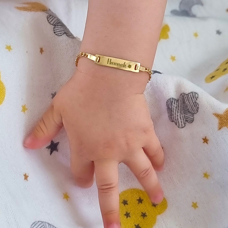 A baby's wrist with a personalized gold ID bracelet engraved with the name 'Hannah'.