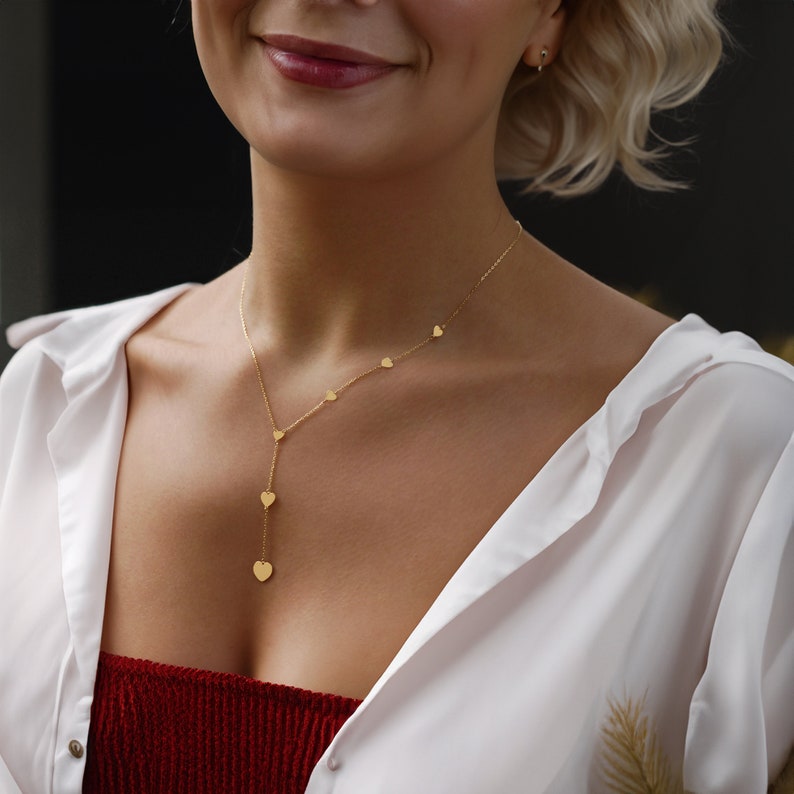 Smiling woman wearing a gold heart Y necklace with a white blouse and maroon top.