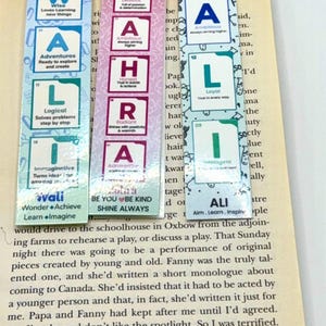 Puede incluir: Tres marcapáginas rectangulares con bloques de letras al estilo de la tabla periódica. El marcapáginas izquierdo deletrea WALI en azul y verde, el central ZAHRA en rosa y rojo, y el derecho ALI en azul y verde. Cada bloque incluye texto descriptivo.