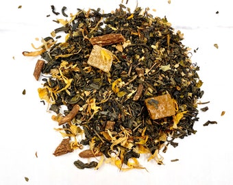 May include: A close-up of a green tea blend with dried fruit pieces, including pineapple and orange, and cinnamon sticks.