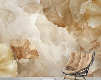 Op de afbeelding: Beige en bruin behang met een herhalend patroon van gestileerde ginkgo bladeren. Een moderne stoel met een gecapitonneerde zitting en een kleine, ronde poef op de voorgrond, wat wijst op een woonkamer of lounge.