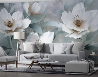 May include: A living room scene featuring a large floral mural with white flowers and muted green leaves. The room includes a white sofa, chair, and ottoman, with a coffee table and a floor lamp. The color palette is soft and neutral.