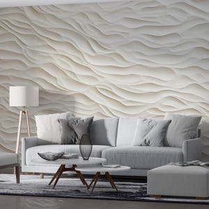 Puede incluir: Un salón moderno con un sofá, una silla y un otomán de color gris claro. Una mesa de centro blanca y una lámpara de pie con una pantalla blanca están frente a una pared texturizada con un patrón de ondas. Una alfombra y cortinas completan la habitación.