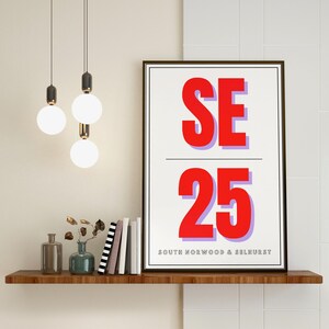 May include: A framed print with a white background and black frame. The print features the text "SE 25" in large red letters with a purple outline. Below the text is the phrase "SOUTH NORWOOD & SELHURST" in black letters.