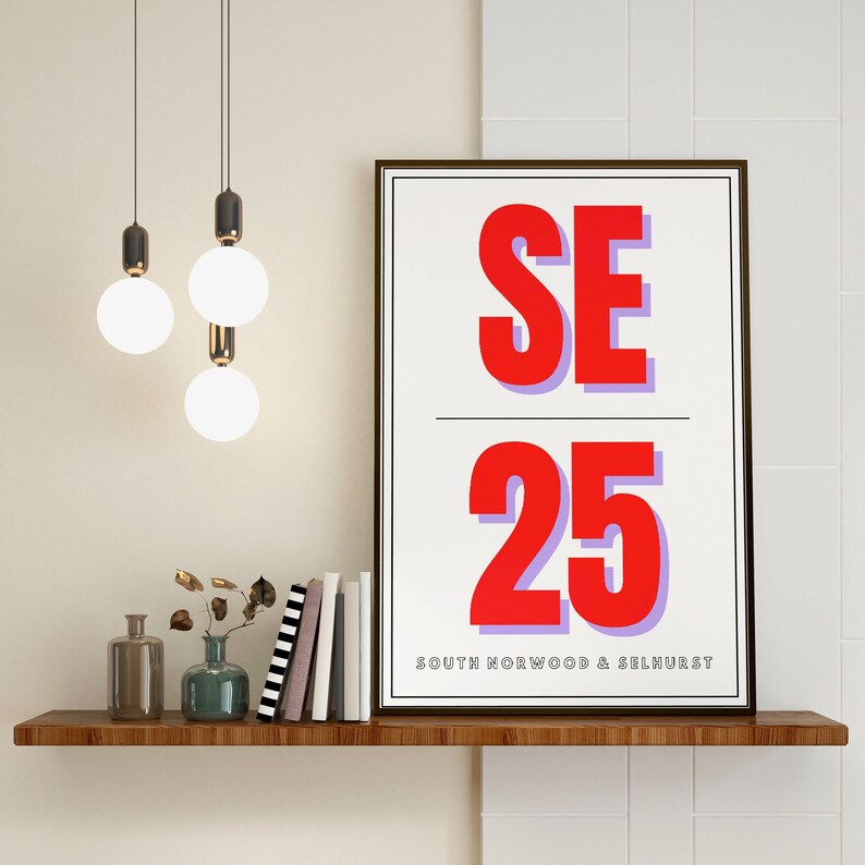 May include: A framed print with a white background and black frame. The print features the text "SE 25" in large red letters with a purple outline. Below the text is the phrase "SOUTH NORWOOD & SELHURST" in black letters.