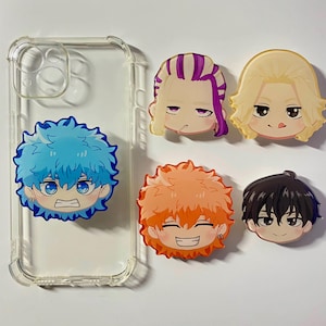 Puede incluir: Cinco amuletos de teléfono de personajes de anime de colores. Los amuletos están hechos de plástico transparente con un diseño impreso. Los personajes tienen diferentes colores de cabello y expresiones.