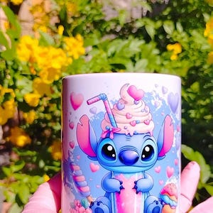 K&ouml;nnte beinhalten: Eine wei&szlig;e Keramiktasse mit einer blauen Comicfigur, die einen rosa Milchshake h&auml;lt. Die Figur hat gro&szlig;e Augen und eine rosa Schleife. Die Tasse ist mit rosa Herzen und einem wei&szlig;en Wirbelmuster verziert.