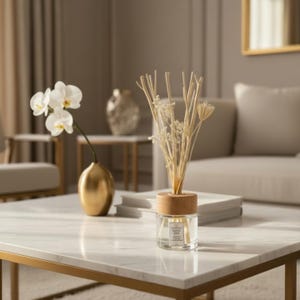 Puede incluir: Un difusor de aceites esenciales de vidrio transparente con una tapa de madera y cañas, sobre una mesa de centro de mármol. Un jarrón dorado con orquídeas blancas y un espejo con marco dorado están en el fondo. La habitación tiene una paleta de colores neutros.