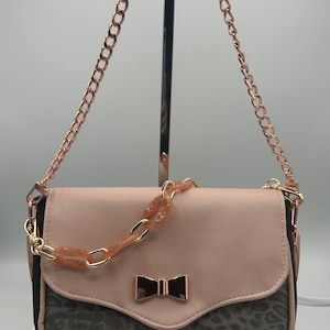 May include: A small pink and brown crossbody bag with a gold chain strap and a gold bow detail.