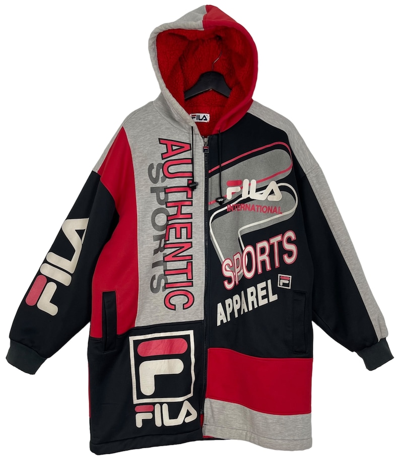 Puede incluir: Chaqueta con capucha Fila con bloques de color en negro, rojo y gris. La chaqueta presenta el logotipo de Fila y las palabras "AUTHENTIC SPORTS APPAREL" en blanco y rosa. Tiene un forro interior rojo y una cremallera completa.