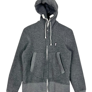 Puede incluir: Una sudadera con capucha con cremallera gris carb&oacute;n con capucha y bolsillos delanteros. La chaqueta presenta una cremallera y cordones blancos, y un peque&ntilde;o logotipo en el pecho. Los pu&ntilde;os y el dobladillo son de un tono gris m&aacute;s oscuro.