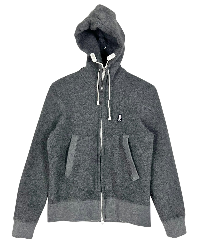 Puede incluir: Una sudadera con capucha con cremallera gris carb&oacute;n con capucha y bolsillos delanteros. La chaqueta presenta una cremallera y cordones blancos, y un peque&ntilde;o logotipo en el pecho. Los pu&ntilde;os y el dobladillo son de un tono gris m&aacute;s oscuro.