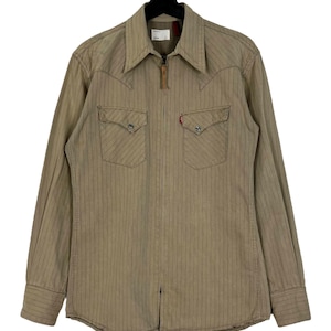 May include: A brown and white striped long-sleeved shirt with a zipper closure. The shirt has two chest pockets with a button closure and a pointed collar.