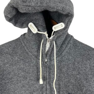 Puede incluir: Una sudadera con capucha gris con cierre de cremallera completo y cordones blancos. La capucha es grande y la sudadera tiene un peque&ntilde;o logotipo bordado de un conejito y una calavera en el pecho.