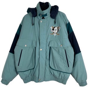 May include: A teal and navy blue winter jacket with a hood. The jacket features the Anaheim Ducks logo on the chest, two front pockets, and a button-up closure. The sleeves have navy blue and teal colour blocking.