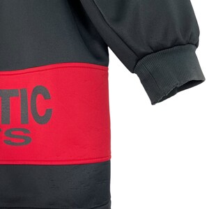 Puede incluir: Sudadera deportiva negra y roja con la palabra "ATHLETIC" impresa en letras negras grandes y en negrita en el pecho. La sudadera tiene un pu&ntilde;o acanalado en la manga. La tela parece ser un material deportivo liso.