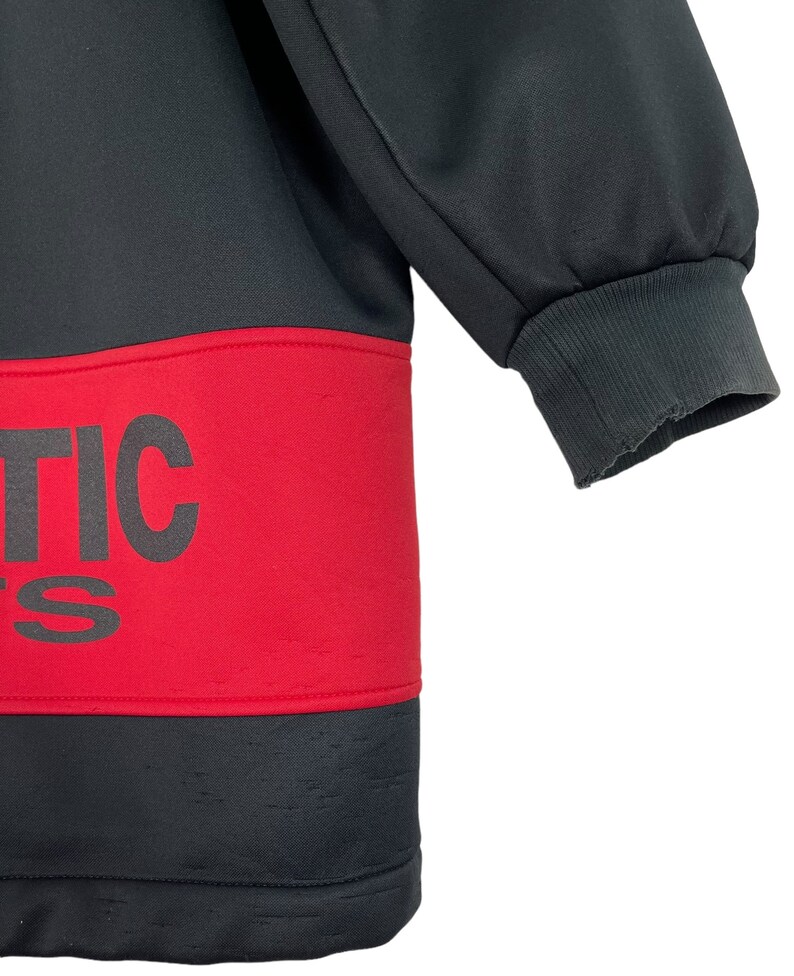 Puede incluir: Sudadera deportiva negra y roja con la palabra "ATHLETIC" impresa en letras negras grandes y en negrita en el pecho. La sudadera tiene un pu&ntilde;o acanalado en la manga. La tela parece ser un material deportivo liso.
