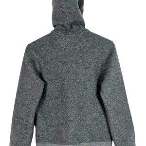 Puede incluir: Una sudadera con capucha gris con capucha con cord&oacute;n y pu&ntilde;os y dobladillo de canal&eacute;. La vista trasera de la sudadera muestra la capucha y la parte superior de la espalda de la prenda. La tela parece ser un material suave similar al forro polar.