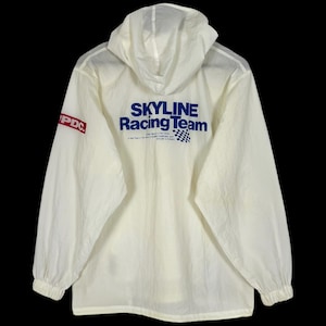 May include: Cream-coloured hooded jacket with long sleeves. The back of the jacket displays the text "SKYLINE Racing Team" in blue, and a chequered flag graphic. The left sleeve has the letters "PDC" in a red box.