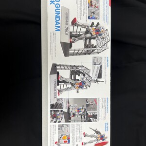 Puede incluir: Caja para un kit de modelo RX-78F00 GUNDAM a escala 1/144. La caja presenta im&aacute;genes del modelo ensamblado en varias poses, con el texto "GUNDAM-DOCK" y texto en japon&eacute;s.