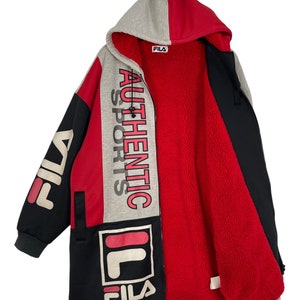 Puede incluir: Chaqueta larga con capucha Fila en negro, rojo y gris. La chaqueta presenta el logotipo de Fila y las palabras "AUTHENTIC SPORTS" en un dise&ntilde;o vertical. El interior est&aacute; forrado con forro polar rojo. La chaqueta tiene cierre de cremallera y capucha.