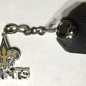 May include: A silver key chain with a gold fleur-de-lis charm and the word "Saints" in silver lettering.