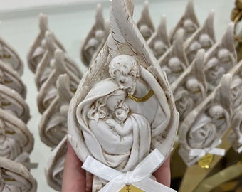 Peut inclure: Figurine religieuse blanche représentant une famille dans des ailes d'ange. La figurine porte une étiquette dorée avec le texte "Julia Rima Vattis" et la date "29 septembre 2024". Un ruban blanc est noué à la base.
