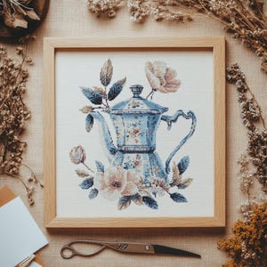 May include: A blue and white ceramic teapot with floral details, surrounded by pink and white flowers, in a wooden frame.