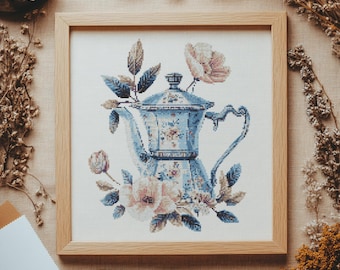 May include: A blue and white ceramic teapot with floral details, surrounded by pink and white flowers, in a wooden frame.