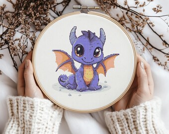 May include: A purple and orange cartoon dragon with big eyes and a friendly smile is embroidered on a white fabric in a round embroidery hoop.