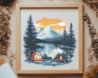 Op de afbeelding: Een kruissteekpatroon met een berglandschap met een meer, een tent en een kampvuur. De scène speelt zich af bij zonsondergang met een warme oranje en gele lucht.