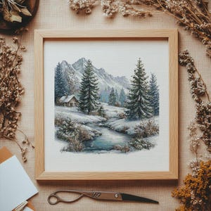 May include: A framed cross-stitch landscape depicting a snowy mountain scene with a cabin, evergreen trees, and a flowing stream. The artwork is set in a light wood frame. The color palette includes shades of white, blue, and green.