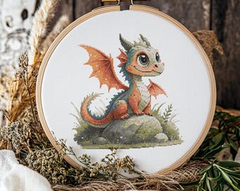 Può includere: Ricamo a punto croce di un drago dei cartoni animati in un telaio di legno. Il drago è arancione, blu e verde, seduto su una roccia con erba verde. Il drago ha grandi occhi e ali arancioni. Il telaio è esposto su uno sfondo di legno rustico.