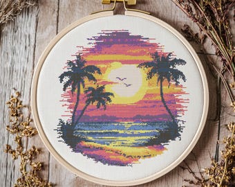 May include: A cross-stitch embroidery hoop depicting a sunset scene with two palm trees, a beach, and a bright orange sun. The colours are vibrant and include shades of pink, orange, yellow, blue, and green.