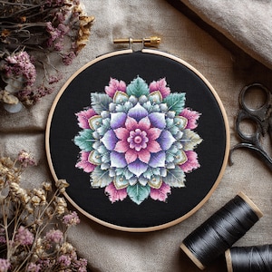 Könnte beinhalten: Fertige Kreuzstich-Stickerei in einem Holzrahmen. Das Design zeigt ein symmetrisches Blumen-Mandala in Rosa-, Lila- und Grüntönen auf schwarzem Hintergrund. Die Abbildung umfasst Trockenblumen, eine Schere und Spulen mit schwarzem Faden.