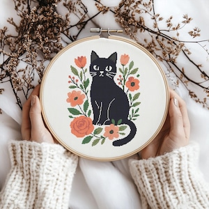 May include: A cross-stitch embroidery hoop featuring a black cat surrounded by orange flowers and green leaves. The cat is centered on a white fabric, held within a wooden hoop. The design has a folk art style.