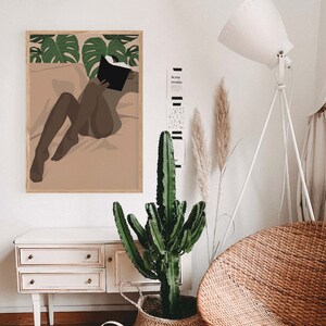 May include: A framed illustration of a person reading a book while lying on a bed with tropical leaves in the background.