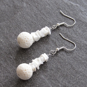 May include: A pair of white earrings with a silver hook. Each earring features a round white bead with a textured surface and a stack of white rectangular beads.