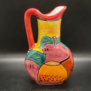 May include: A hand-painted ceramic pitcher with a red handle and a yellow, orange, red, and green fruit design.