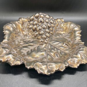 May include: Silver grape leaf dish with a cluster of grapes in the center. The dish is intricately detailed with a textured leaf design.
