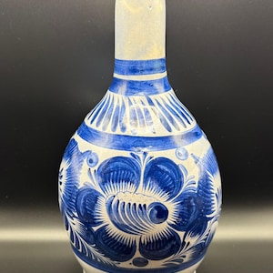 May include: A hand-painted ceramic vase with a white base and a long neck. The vase features a blue floral design around the body and neck. The vase is approximately 8 inches tall.