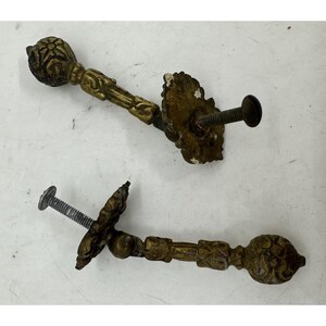 May include: Two antique brass door handles with ornate floral designs and a screw attachment. The handles are in good condition with a worn patina.