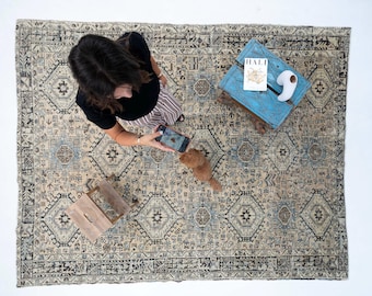 May include: A large rectangular area rug featuring a complex, distressed pattern in shades of beige, light blue, and dark charcoal. The design includes repeating geometric medallions, intricate borders, and small tribal-inspired motifs throughout.