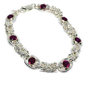 May include: A silver chain bracelet featuring a complex woven link pattern interspersed with six round, deep magenta-coloured gemstones set in polished silver bezels. The bracelet includes a secure silver clasp mechanism at the top of the loop.