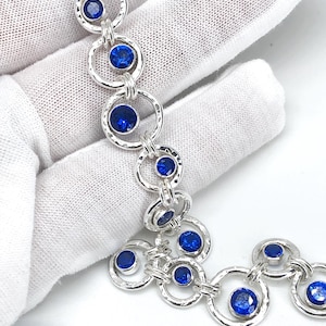 May include: A silver bracelet with a series of linked circles, each set with a bright blue gemstone. The bracelet has a hammered finish. The round gemstones are set within the silver circles, creating a striking contrast.