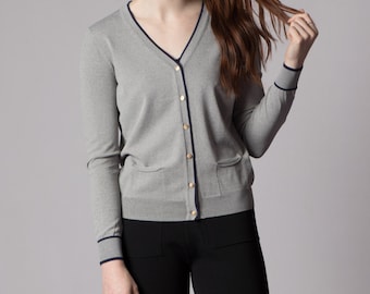 May include: A gray cardigan with a navy blue trim and gold buttons. The cardigan has a v-neck and long sleeves.