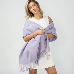 May include: A light purple pashmina shawl with fringe. The shawl is draped around a person's shoulders and is made of a soft, luxurious fabric.