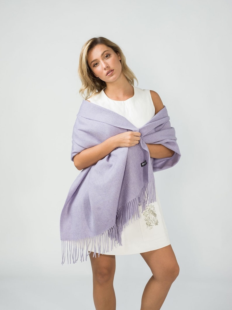 May include: A light purple pashmina shawl with fringe. The shawl is draped around a person's shoulders and is made of a soft, luxurious fabric.